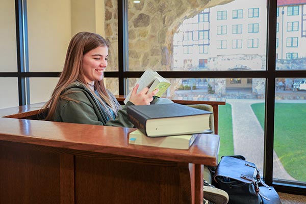student studying in front of a window with carter hall in background