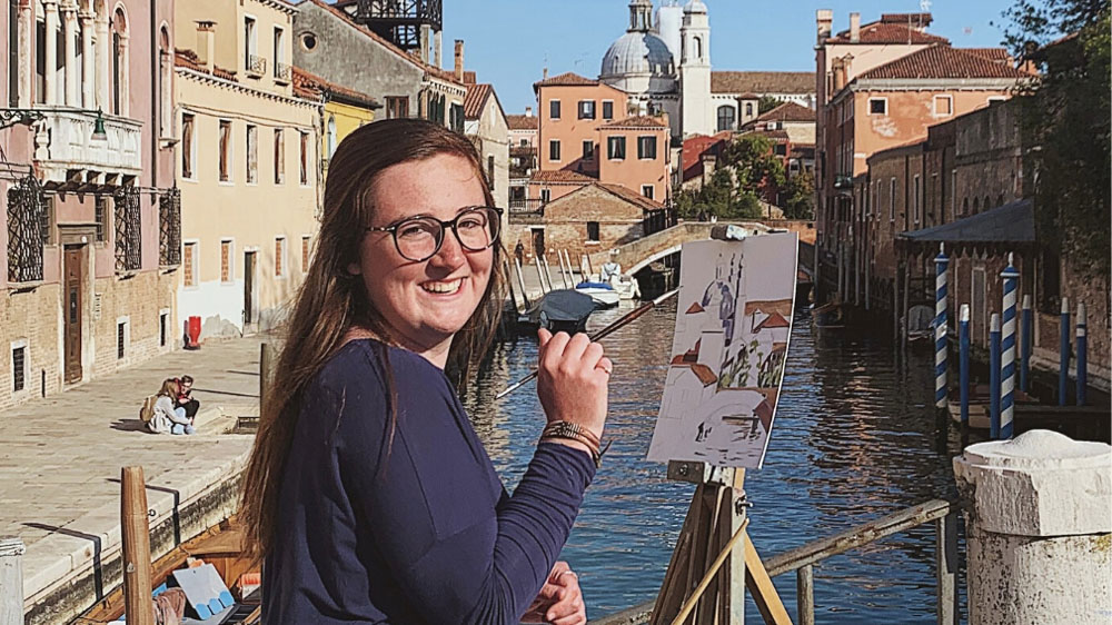 student painting a city scene with river in background