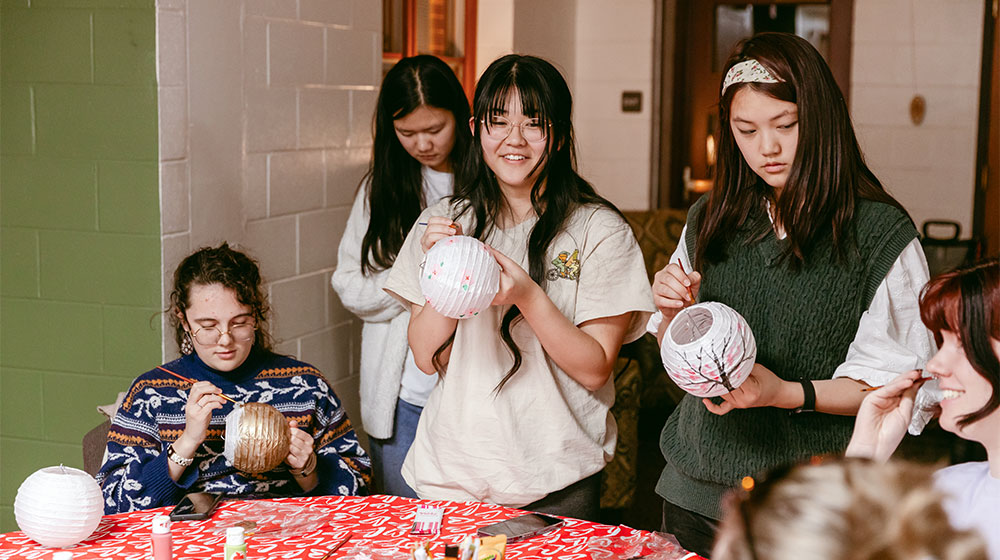 A group of students painting paper lanterns together at a table.
