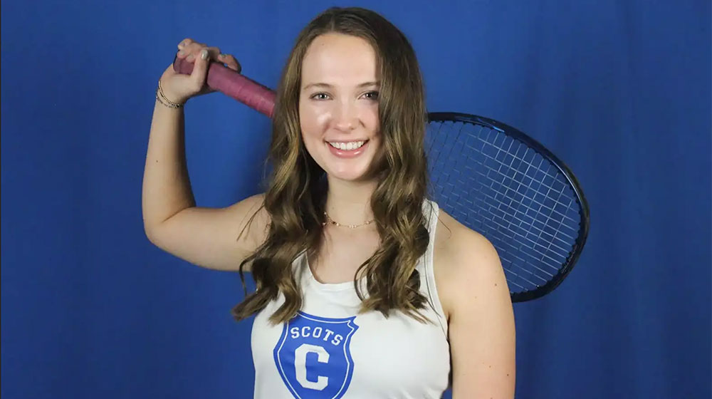 Smiling tennis player holding a racket over her shoulder against a blue background