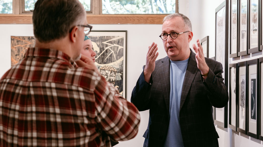 ned bustard talking with gallery visitors with his art displayed on the walls