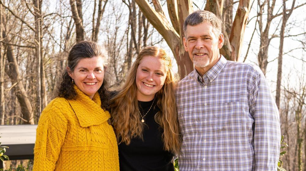 Mother, daughter, and father smiling outdoors among bare trees