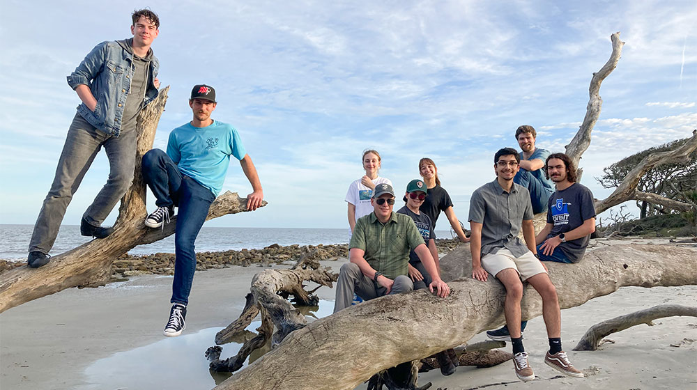 students and faculty sitting in drift wood on beach