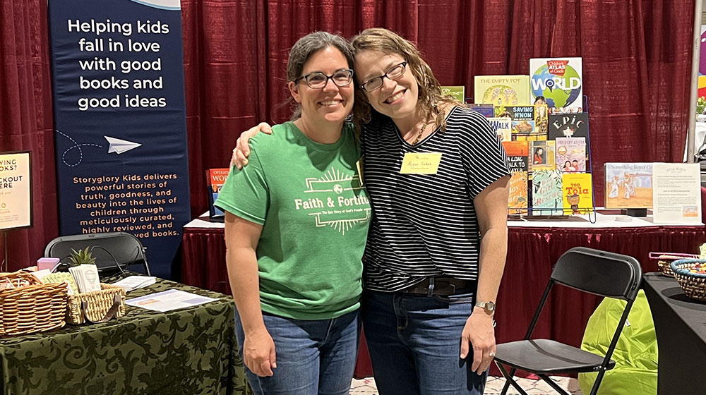 two woman standing in a tradeshow booth surrounded my books