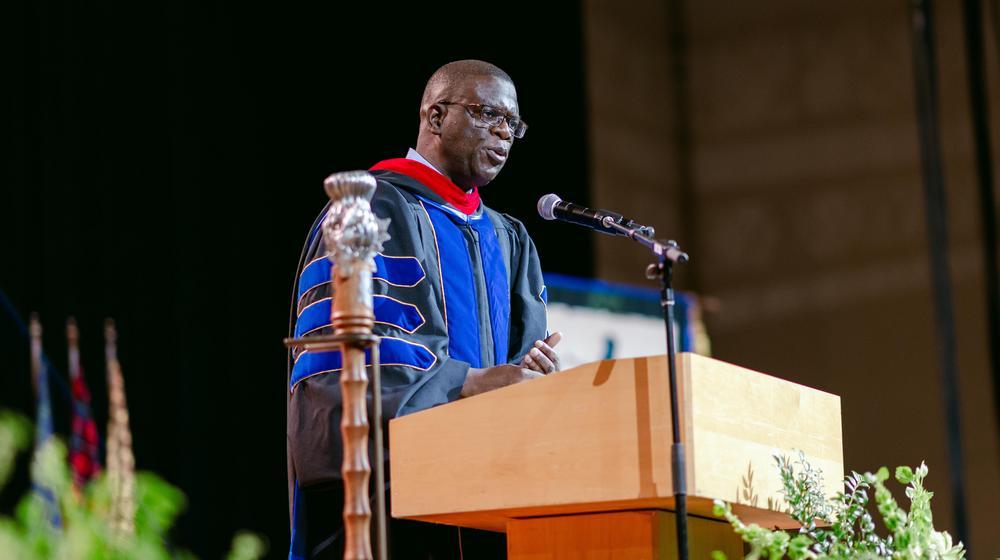 Speaker in academic gown addressing audience from a podium at commencement
