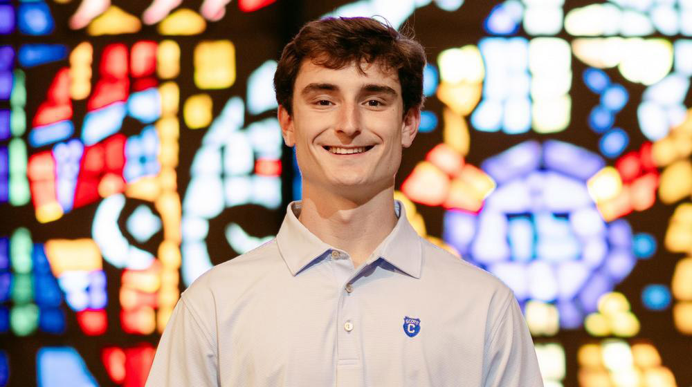 Smiling young man in a light polo shirt standing in front of a colorful stained glass window