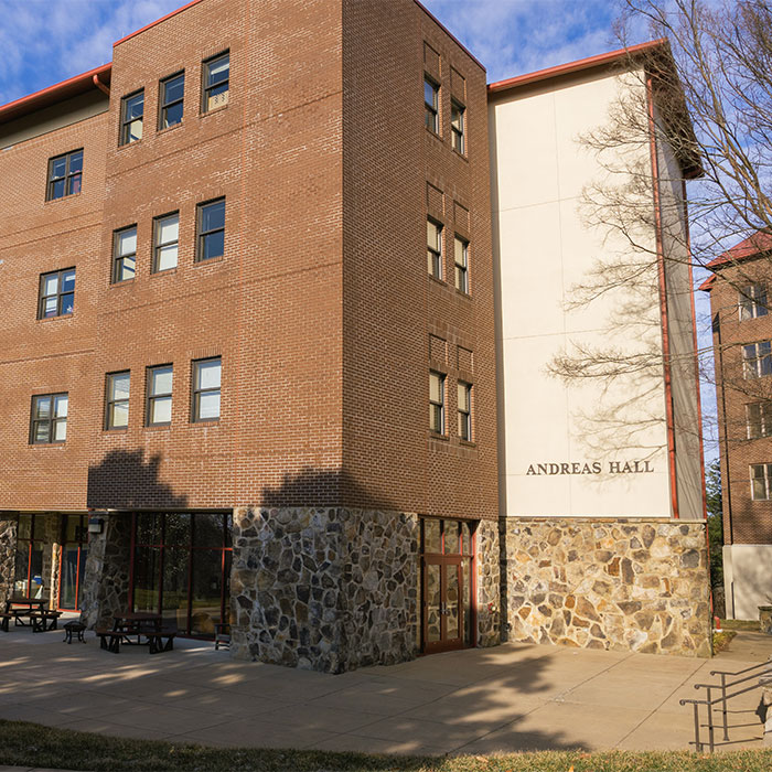 Exterior view of 安德烈亚斯 Hall, a brick dorm building with a stone base and large windows.