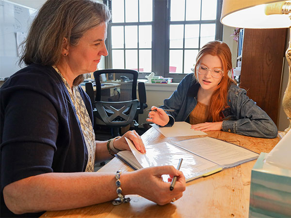 A staff member and a student seated at a desk, reviewing documents together in an office.