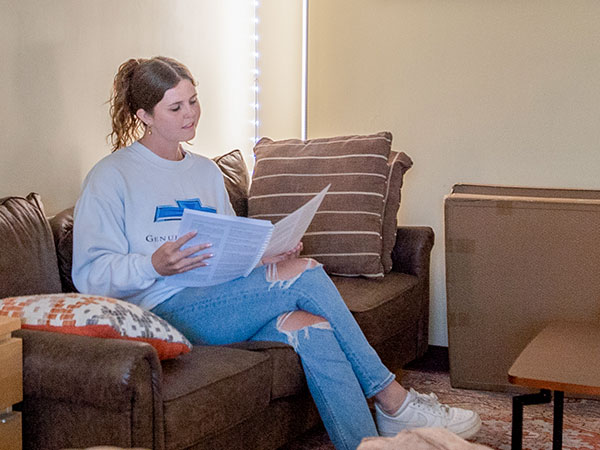 A student sitting on a couch, reviewing papers in a relaxed setting.